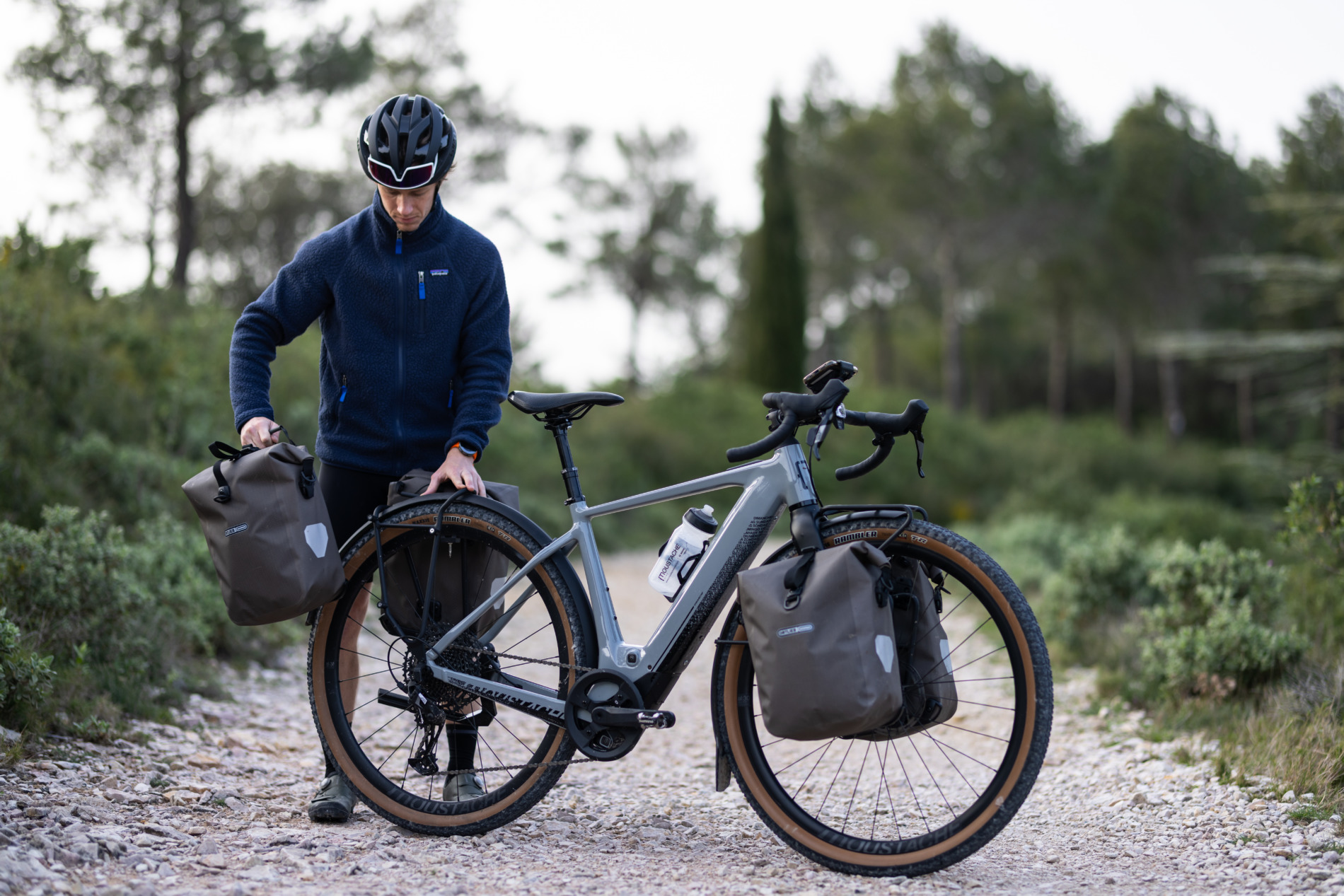 Ein fahrer der seine Ortlieb Tasche an das Moustache Gravel Bike befestigt